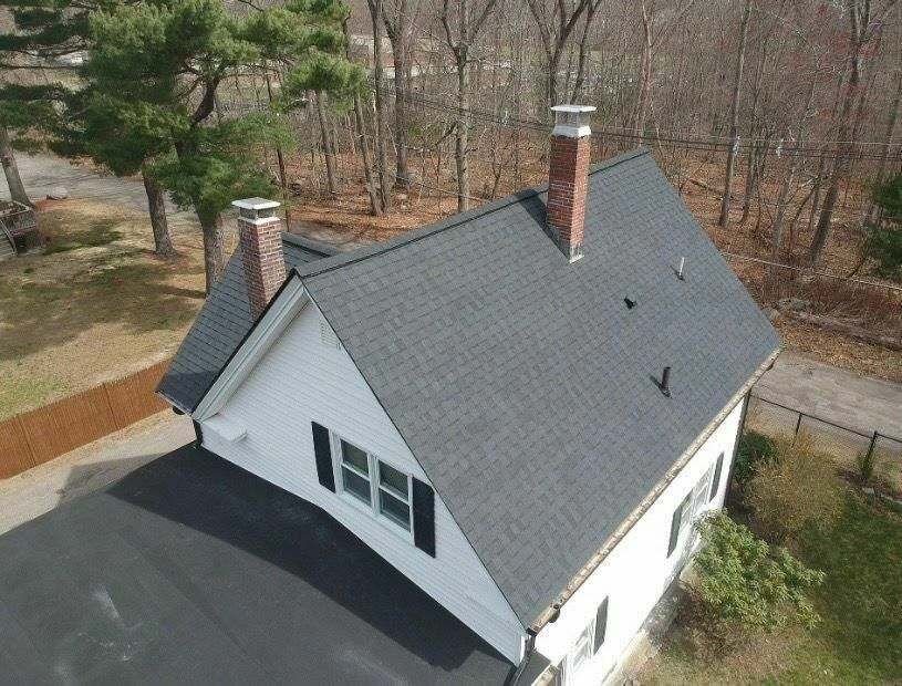 White cape-style home with a new dark roof and chimney