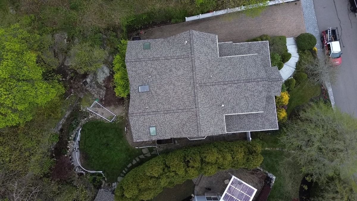 Aerial view of a completed gray shingle roof surrounded by trees